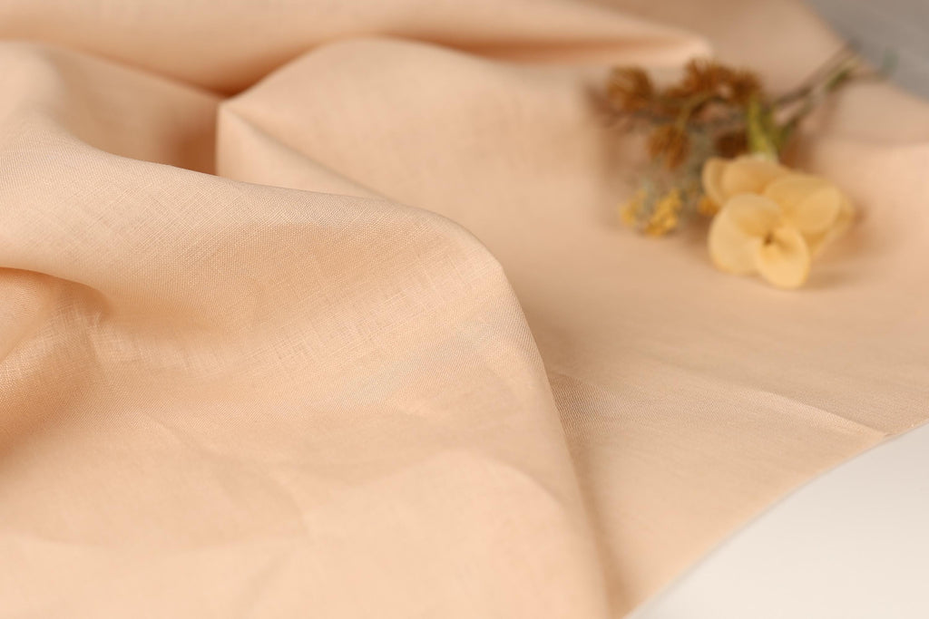 A close-up image of a soft, light peach fabric with a delicate yellow flower resting on it.
