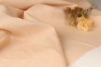 A close-up image of a soft, light peach fabric with a delicate yellow flower resting on it.