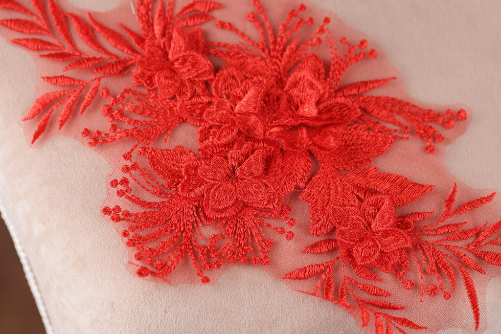a close-up view of a delicate red embroidered flower design on a fabric surface.
