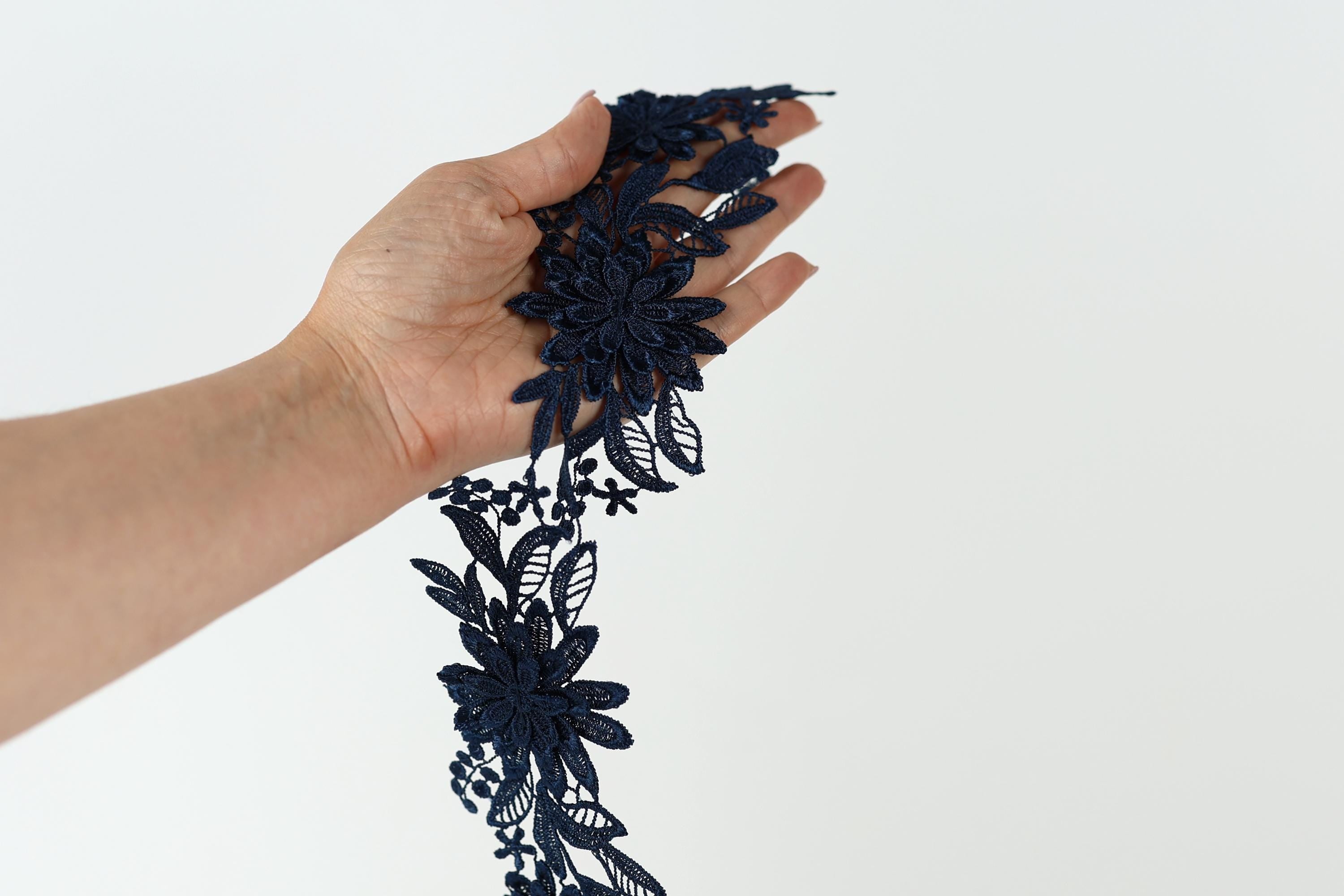 A hand holding a piece of blue lace with intricate floral patterns.