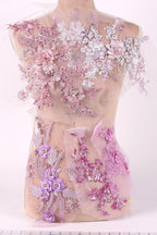 A mannequin torso covered in a delicate, intricate lace and floral embroidery in shades of pink and purple.