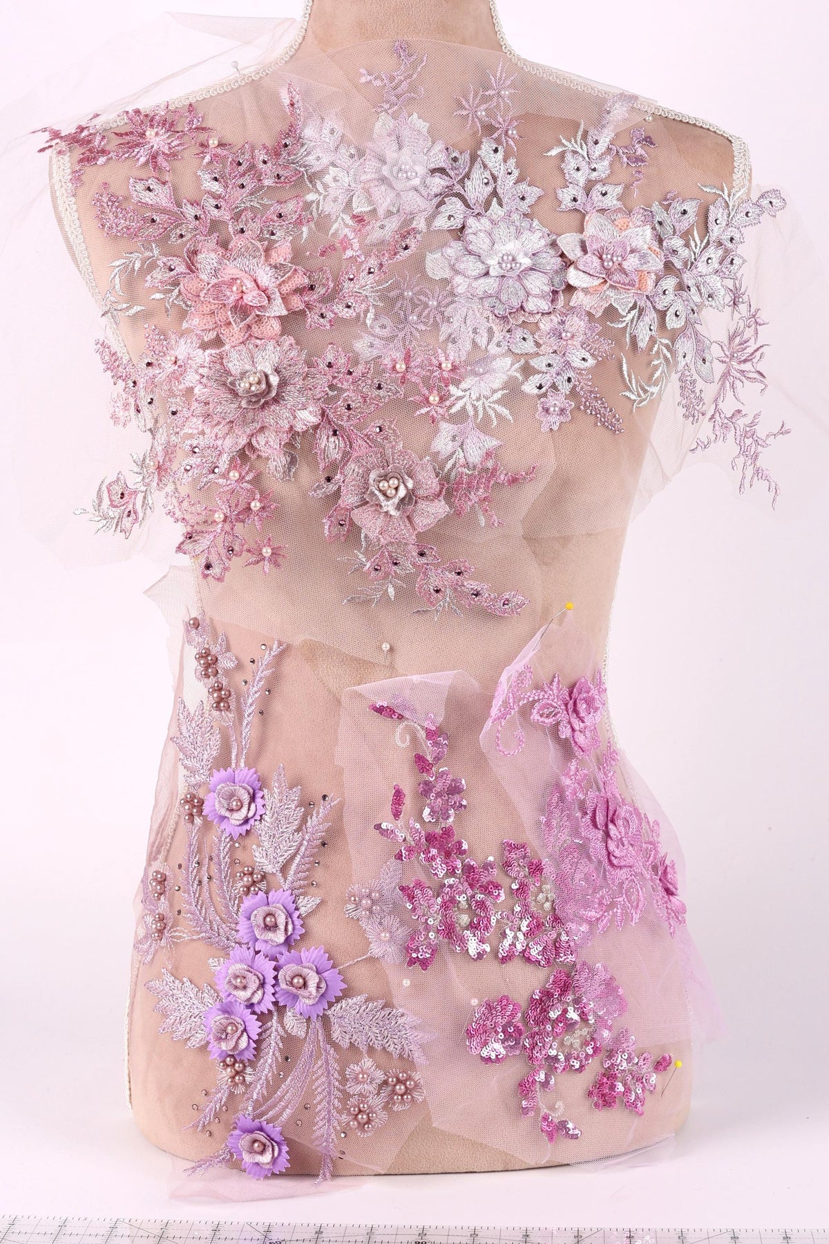 A mannequin torso covered in a delicate, intricate lace and floral embroidery in shades of pink and purple.