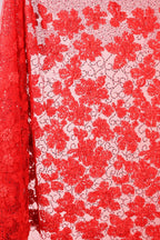 a close-up view of a red fabric with a floral pattern. The fabric appears to be made of a sheer material, with a repeating pattern of red flowers and leaves. The fabric is displayed in a vertical orientation, with the left side of the fabric partially visible.