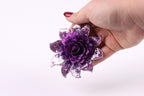 A hand holding a purple sequin flower against a white background.