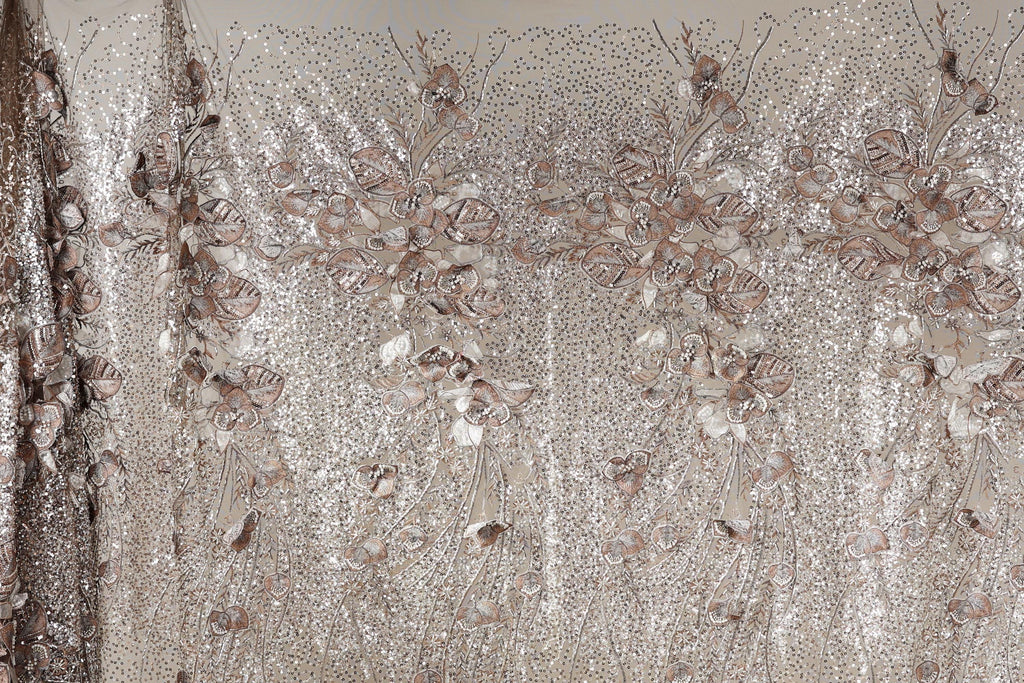 a close-up view of a fabric with a floral pattern, including various shades of brown and beige. The fabric appears to be made of sequin material, giving it a shiny and decorative appearance.