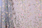 a close-up view of a fabric with a floral pattern, including various shades of pink, green, and white flowers and leaves. The fabric appears to be made of a sheer material, giving it a delicate and airy appearance. The pattern is intricate and detailed, with the flowers and leaves arranged in a way that creates a visually appealing and textured design.