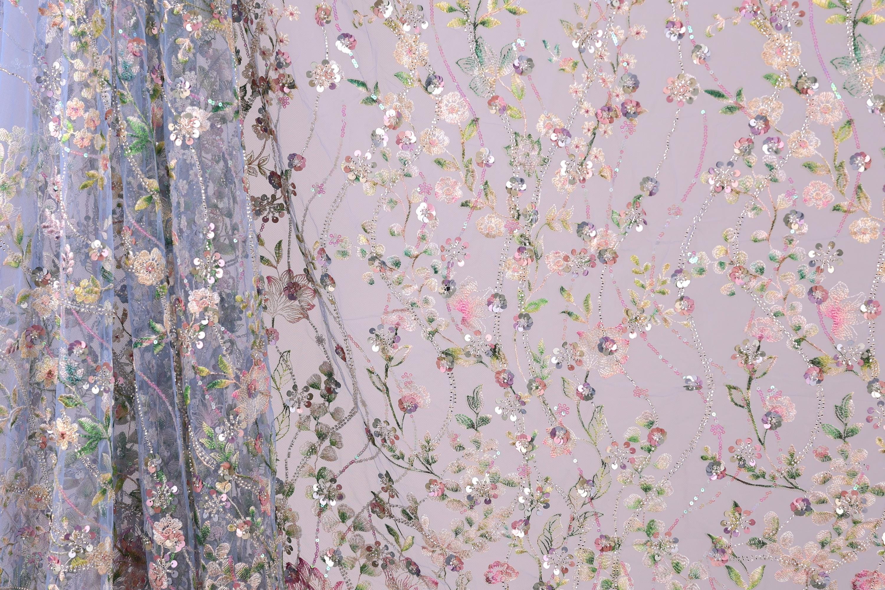a close-up view of a fabric with a floral pattern, including various shades of pink, green, and white flowers and leaves. The fabric appears to be made of a sheer material, giving it a delicate and airy appearance. The pattern is intricate and detailed, with the flowers and leaves arranged in a way that creates a visually appealing and textured design.