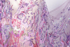 The image is a close-up view of a fabric with a floral pattern, featuring a mix of pink, purple, and green colors. The fabric appears to be made of sequins or other embellishments, adding a sparkly and decorative touch.