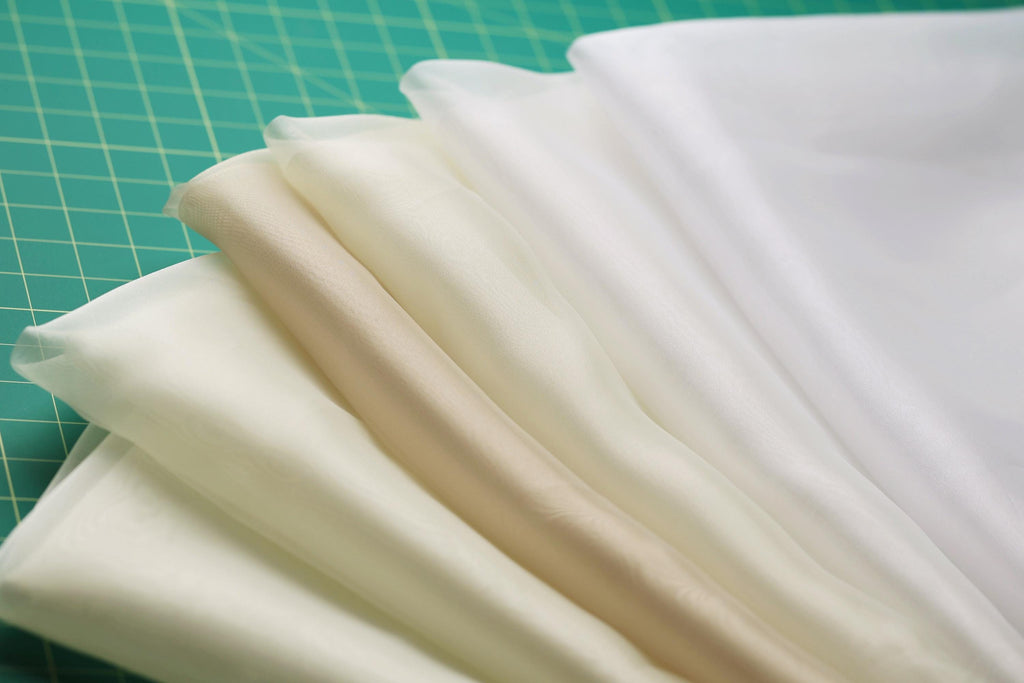 A close-up view of a collection of fabric swatches in various shades of white and beige, arranged on a green surface.