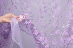 A hand holding a piece of fabric with a floral pattern of purple flowers against a purple background.