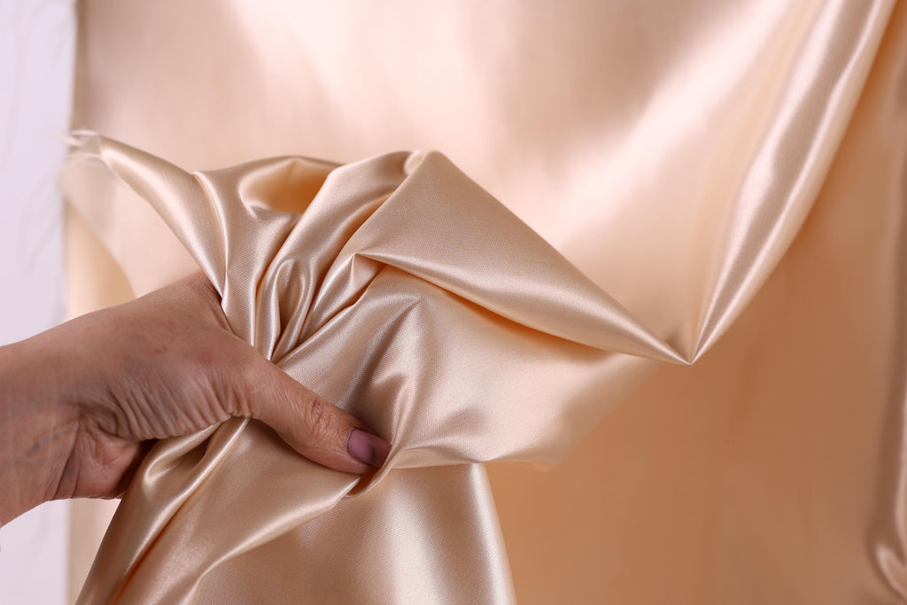 A hand is holding a piece of light pink satin fabric, which appears to be a close-up view of the material.