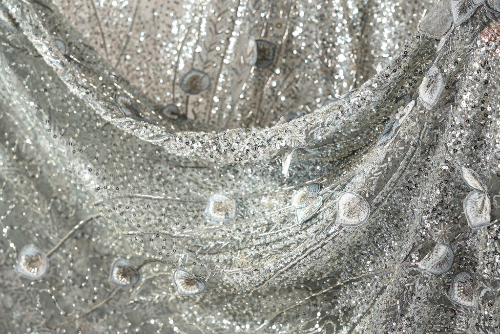The image is a close-up of a silver sequin fabric with a floral pattern.