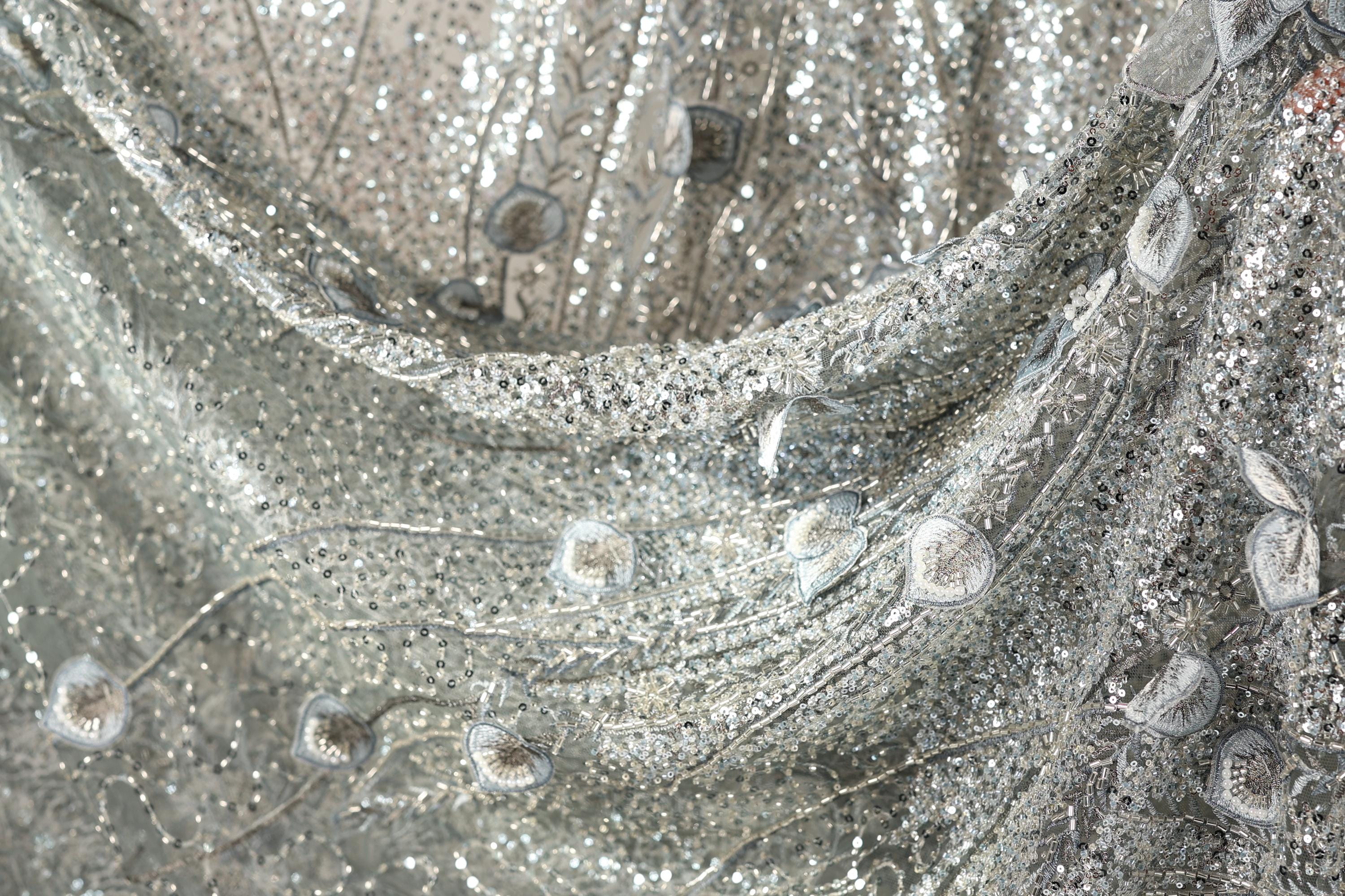 The image is a close-up of a silver sequin fabric with a floral pattern.