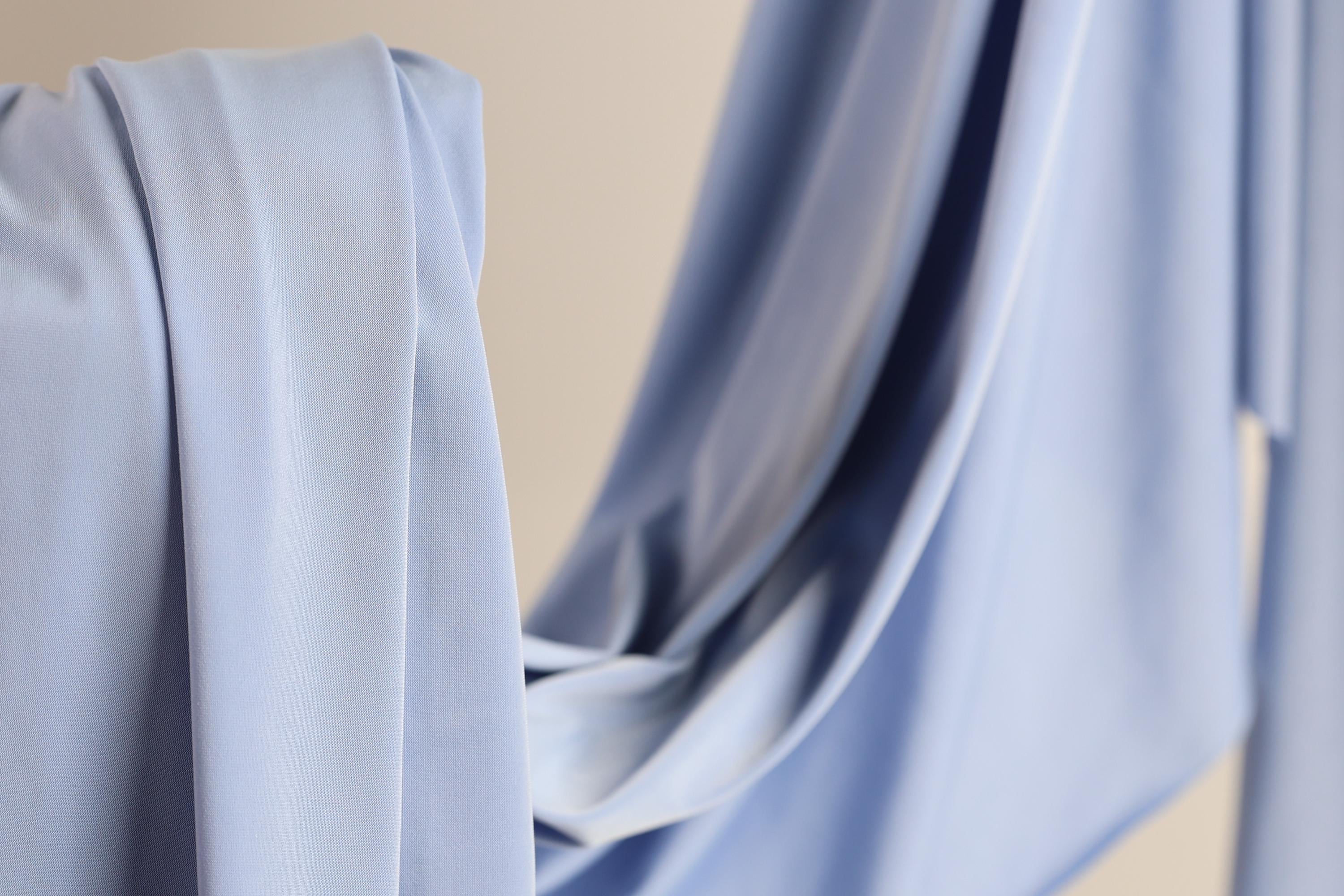 A close-up view of a light blue fabric, possibly a piece of clothing or a textile, with a soft, flowing texture.