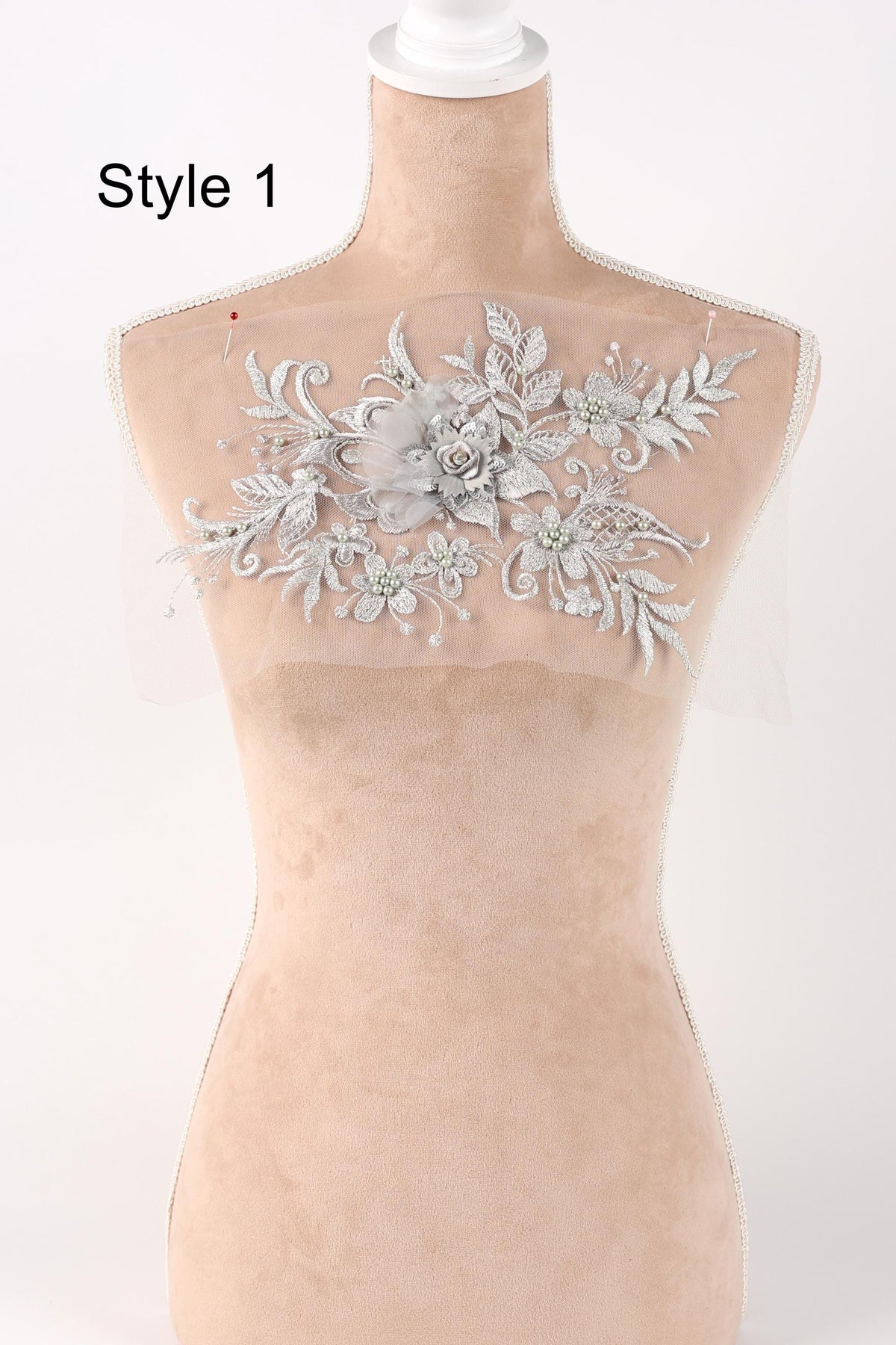 A mannequin with a decorative floral embroidery on its bust area, featuring a variety of white and silver floral designs.