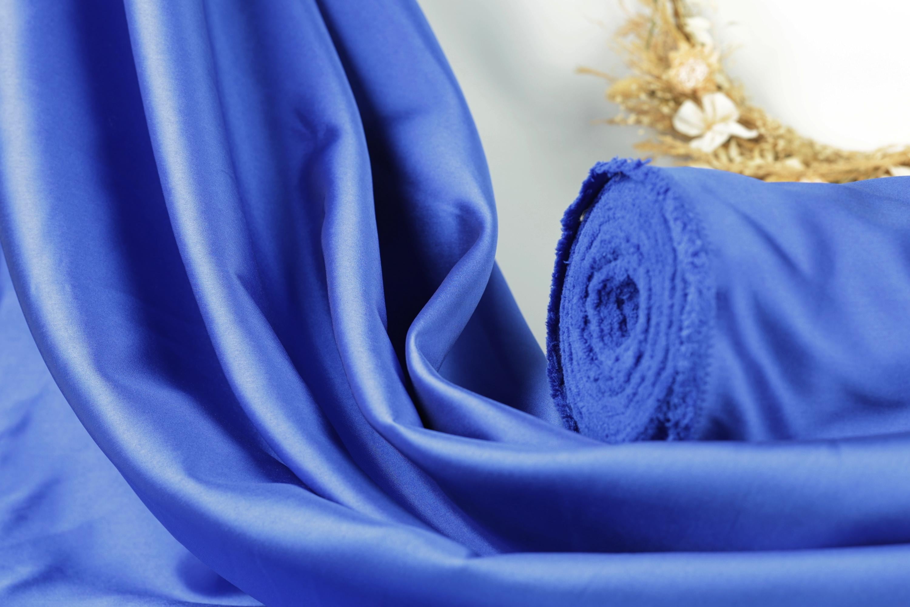 A close-up view of a blue satin fabric, with a rolled-up piece of the fabric visible in the background.