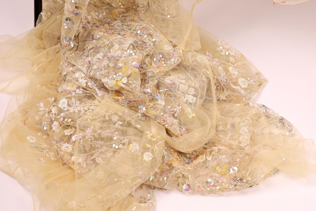 a close-up view of a delicate, beige-colored fabric with intricate floral embroidery and sequins. The fabric appears to be a sheer, sheer-like material, which adds a soft, delicate touch to the overall appearance.