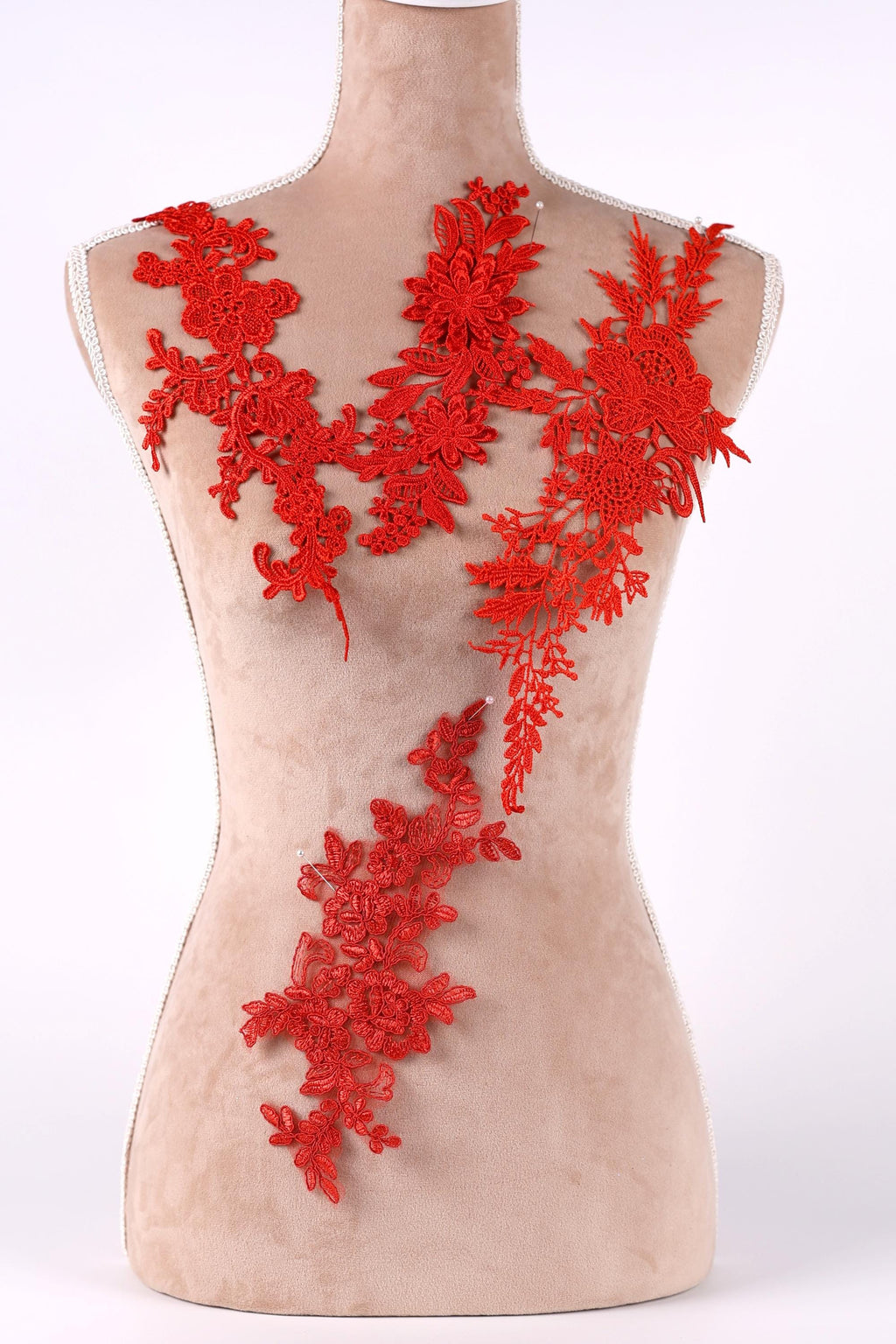 A mannequin torso with red floral and leaf-like embroidery pieces attached to it.
