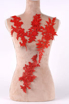 A mannequin torso with red floral and leaf-like embroidery pieces attached to it.