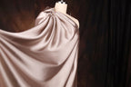 A mannequin wearing a flowing, draped fabric in a light pink color, set against a dark background.