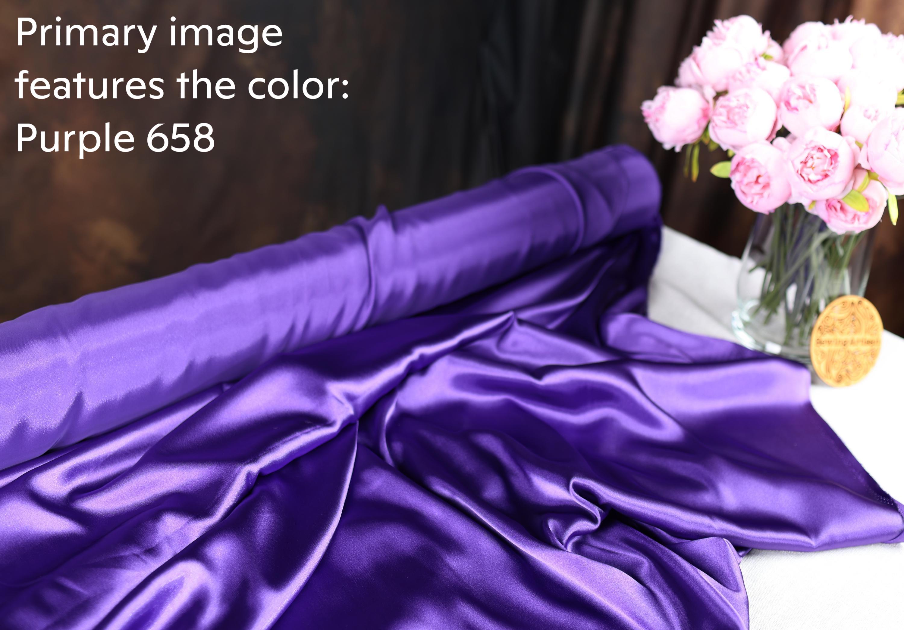 a roll of purple satin fabric, a vase of pink flowers, and a wooden plaque on a table.