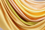 a close-up view of a collection of colorful, flowing fabric swatches in various shades of yellow, orange, and green.