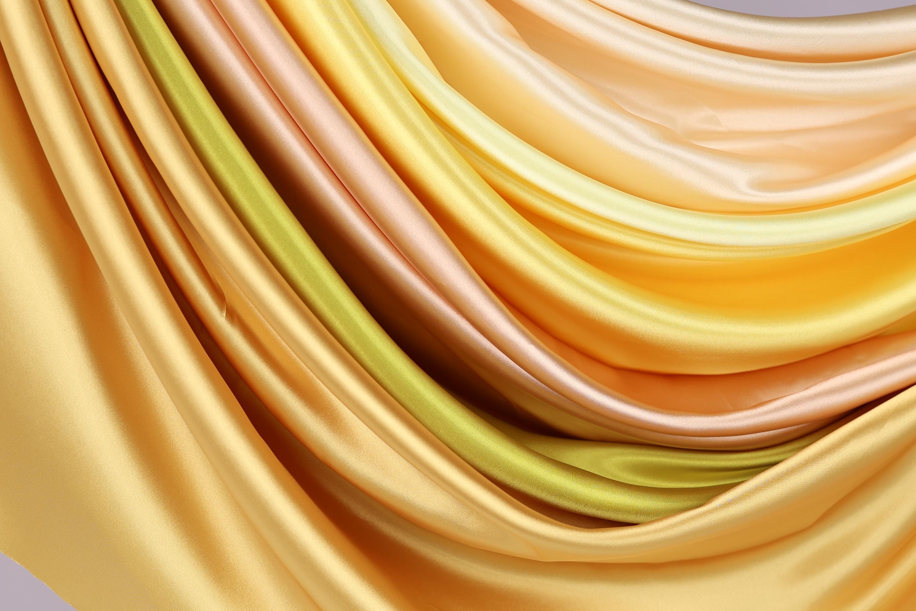 a close-up view of a collection of colorful, flowing fabric swatches in various shades of yellow, orange, and green.