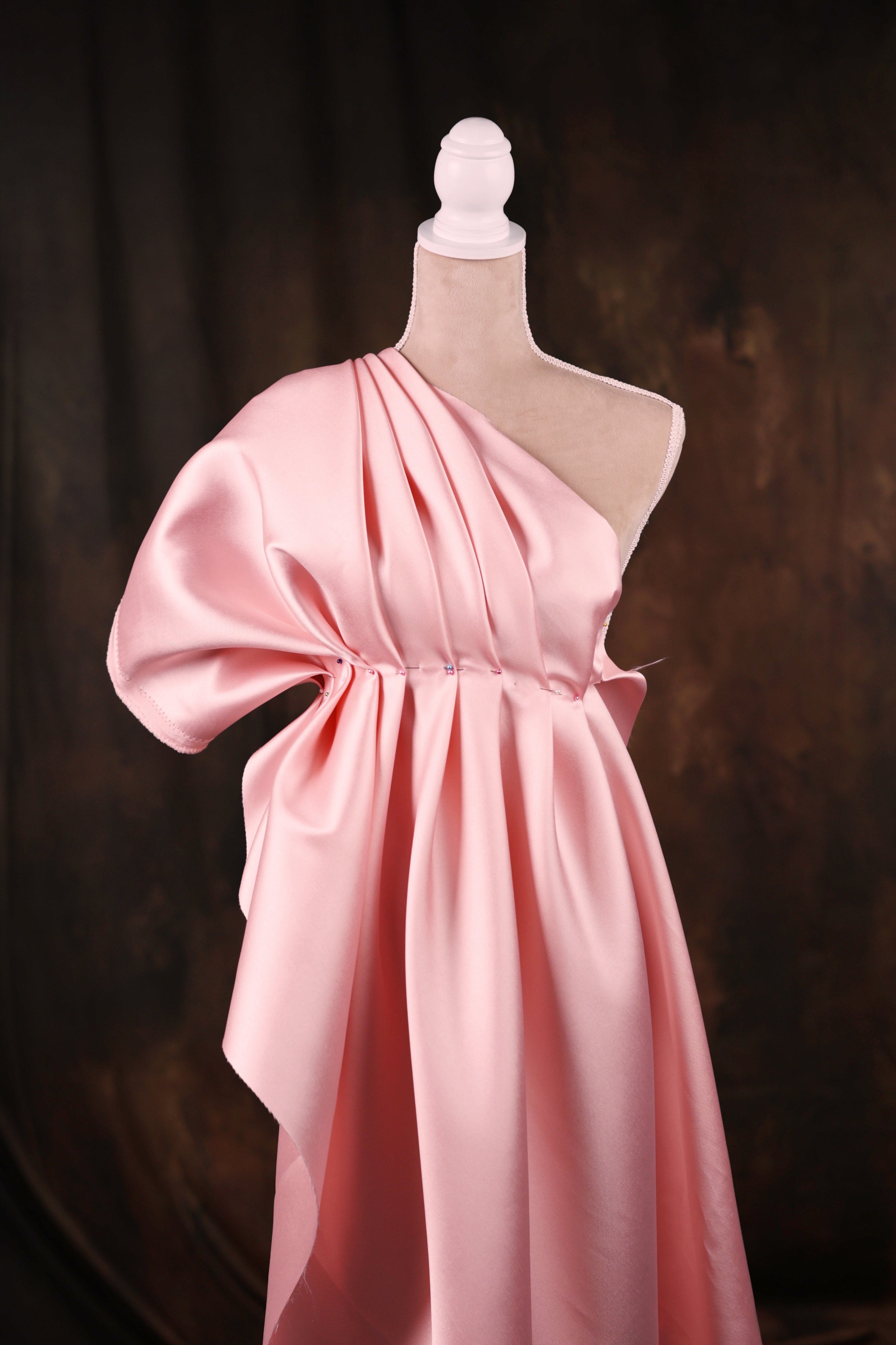 A pink one-shoulder dress displayed on a mannequin against a dark background.