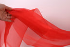 A hand is holding a red fabric, which appears to be a sheer or sheer-like material. The hand is positioned in the center of the image, with the fabric extending towards the right side.