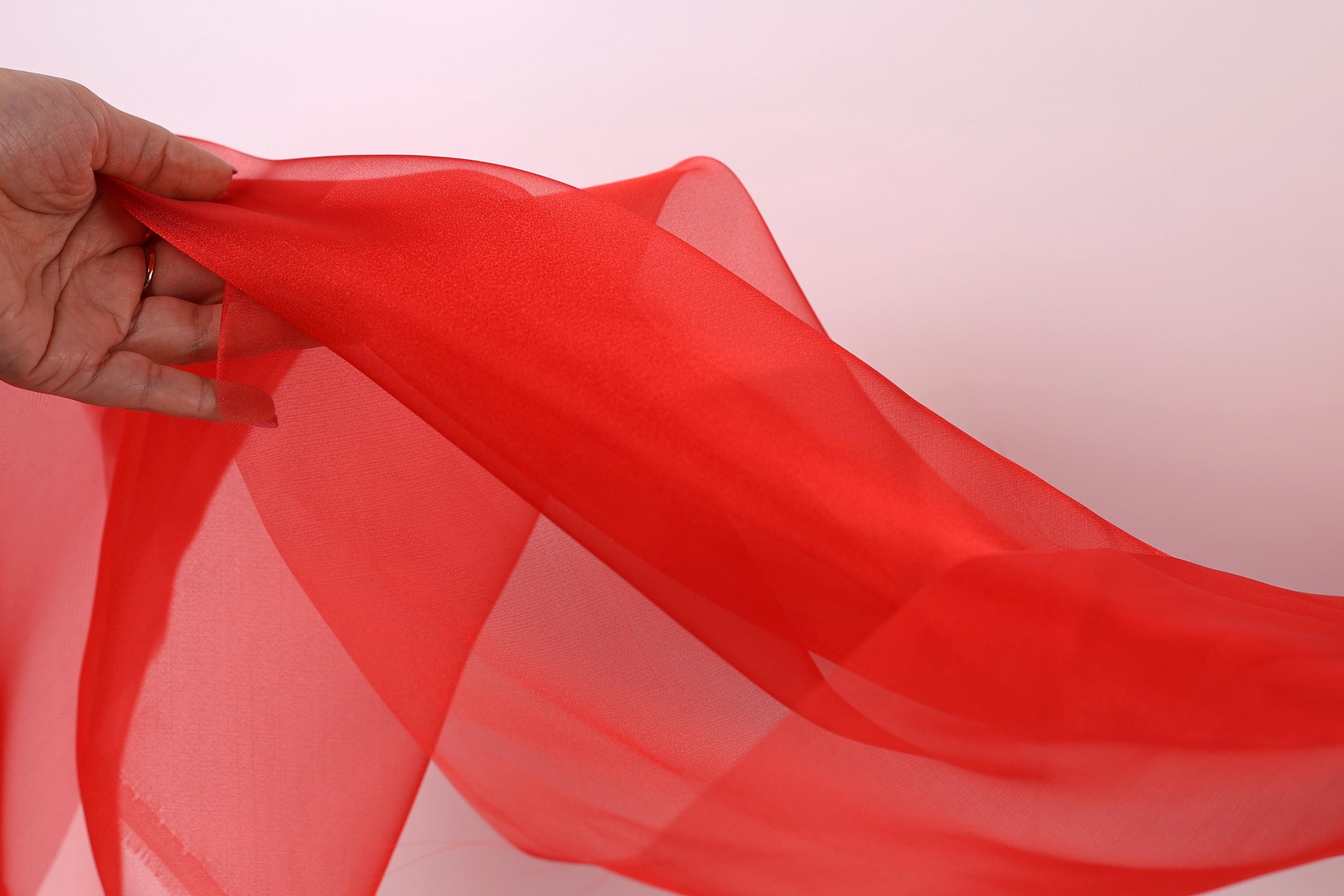 A hand is holding a red fabric, which appears to be a sheer or sheer-like material. The hand is positioned in the center of the image, with the fabric extending towards the right side.