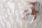 A hand is holding a delicate white lace fabric with intricate floral embroidery.