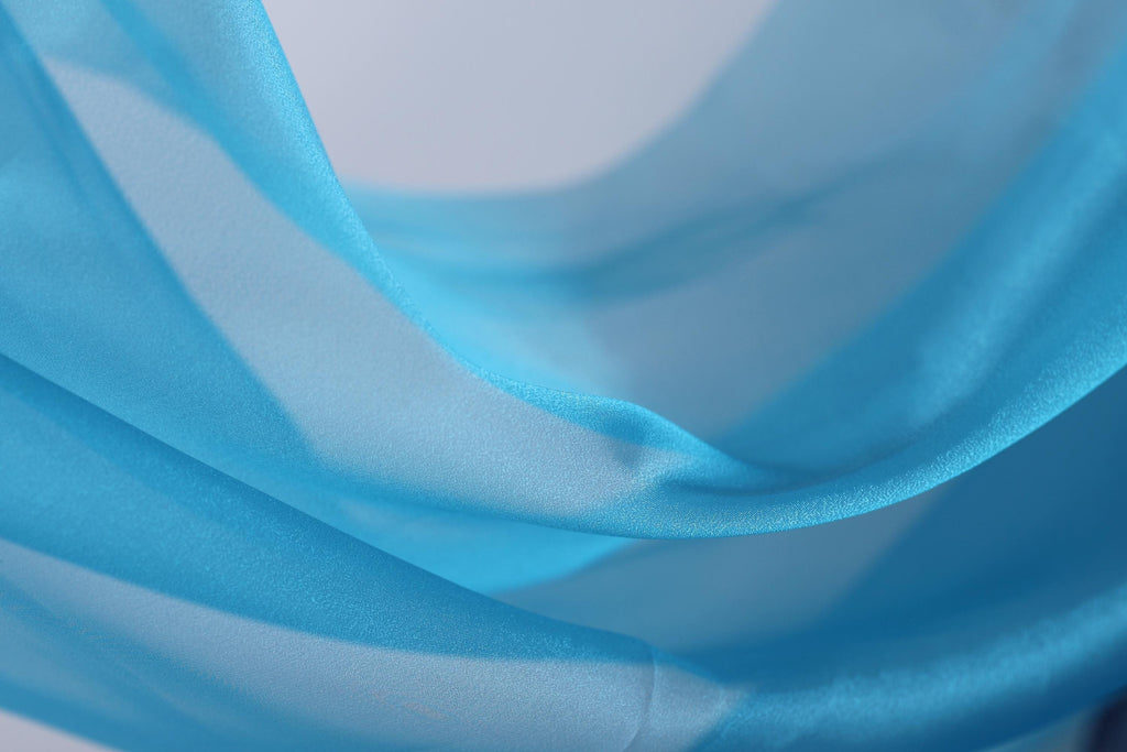 A close-up view of a blue fabric, possibly silk or chiffon, with a soft, flowing texture.