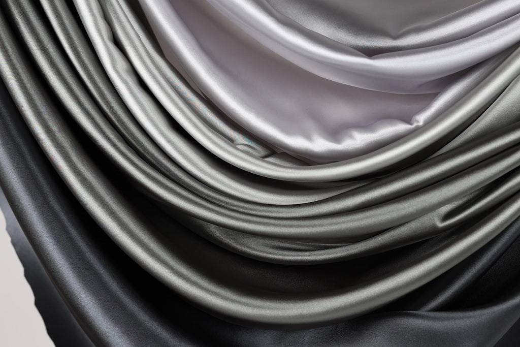 a close-up view of a pile of shiny, silky-looking fabric in shades of gray and black.