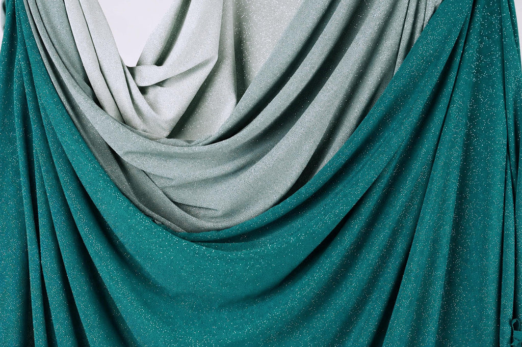 a close-up view of a fabric with a shimmering, metallic texture in shades of green and gray. The fabric appears to be draped or folded, creating a sense of depth and dimension.