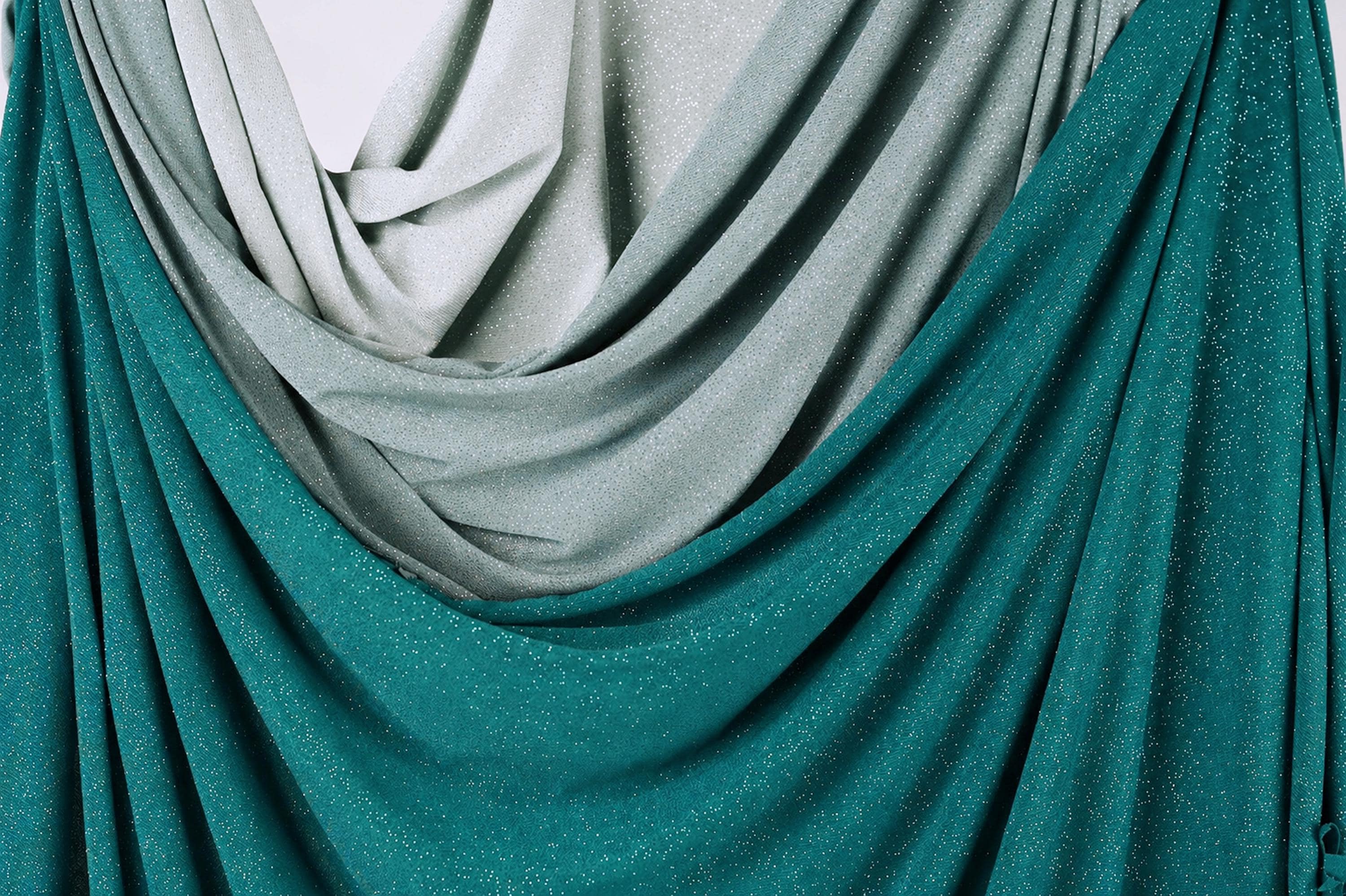 a close-up view of a fabric with a shimmering, metallic texture in shades of green and gray. The fabric appears to be draped or folded, creating a sense of depth and dimension.