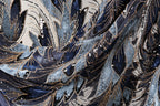 The image is a close-up view of a fabric with a complex, intricate pattern of blue and black sequins and beads. The pattern appears to be a mix of different textures and colors, creating a visually striking and detailed design.