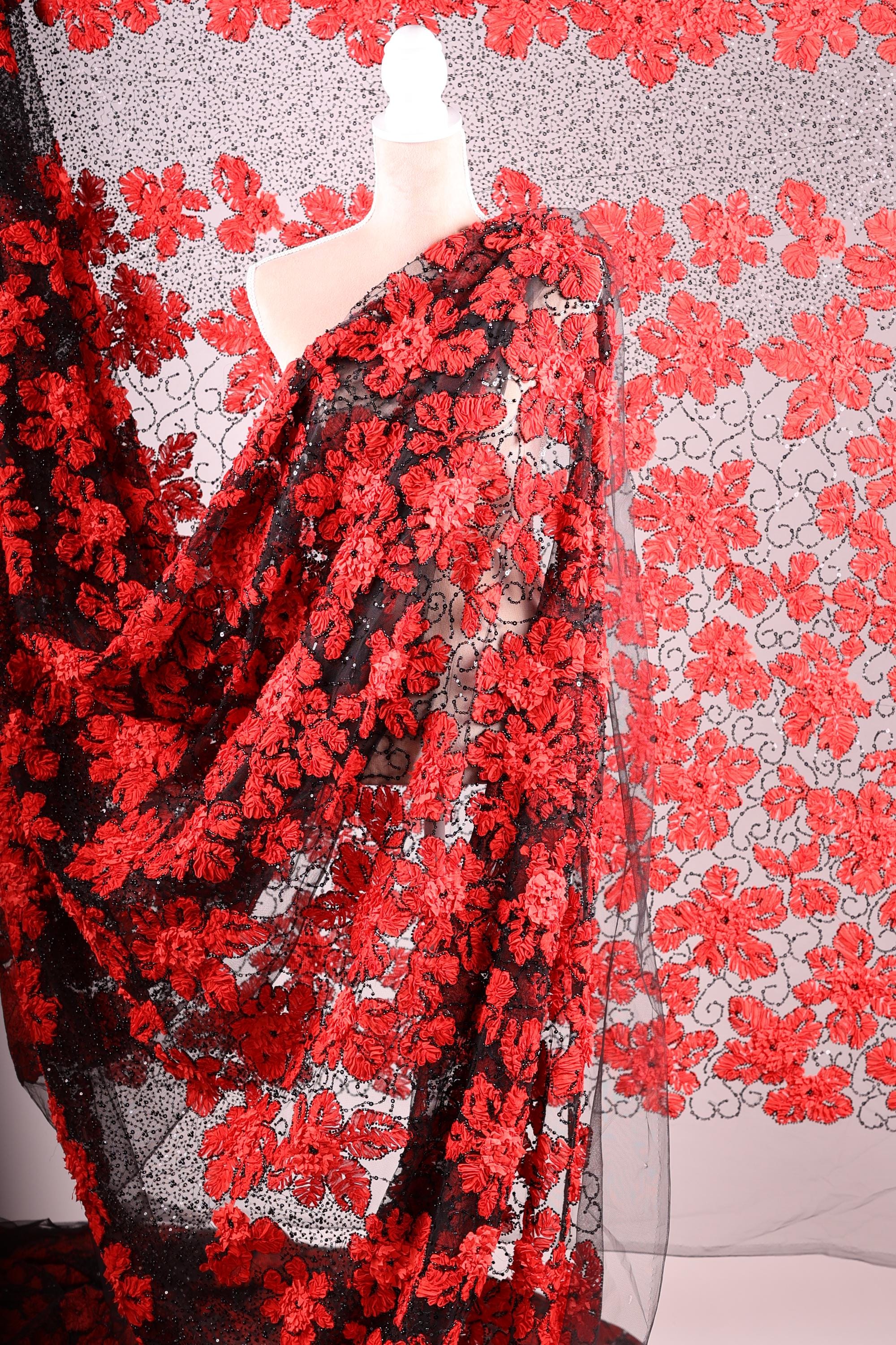 a close-up view of a fabric with a striking red floral pattern. The fabric appears to be a sheer material, with a black and red color scheme. The pattern consists of numerous red flowers arranged in a repeating design, creating a visually captivating and vibrant appearance.