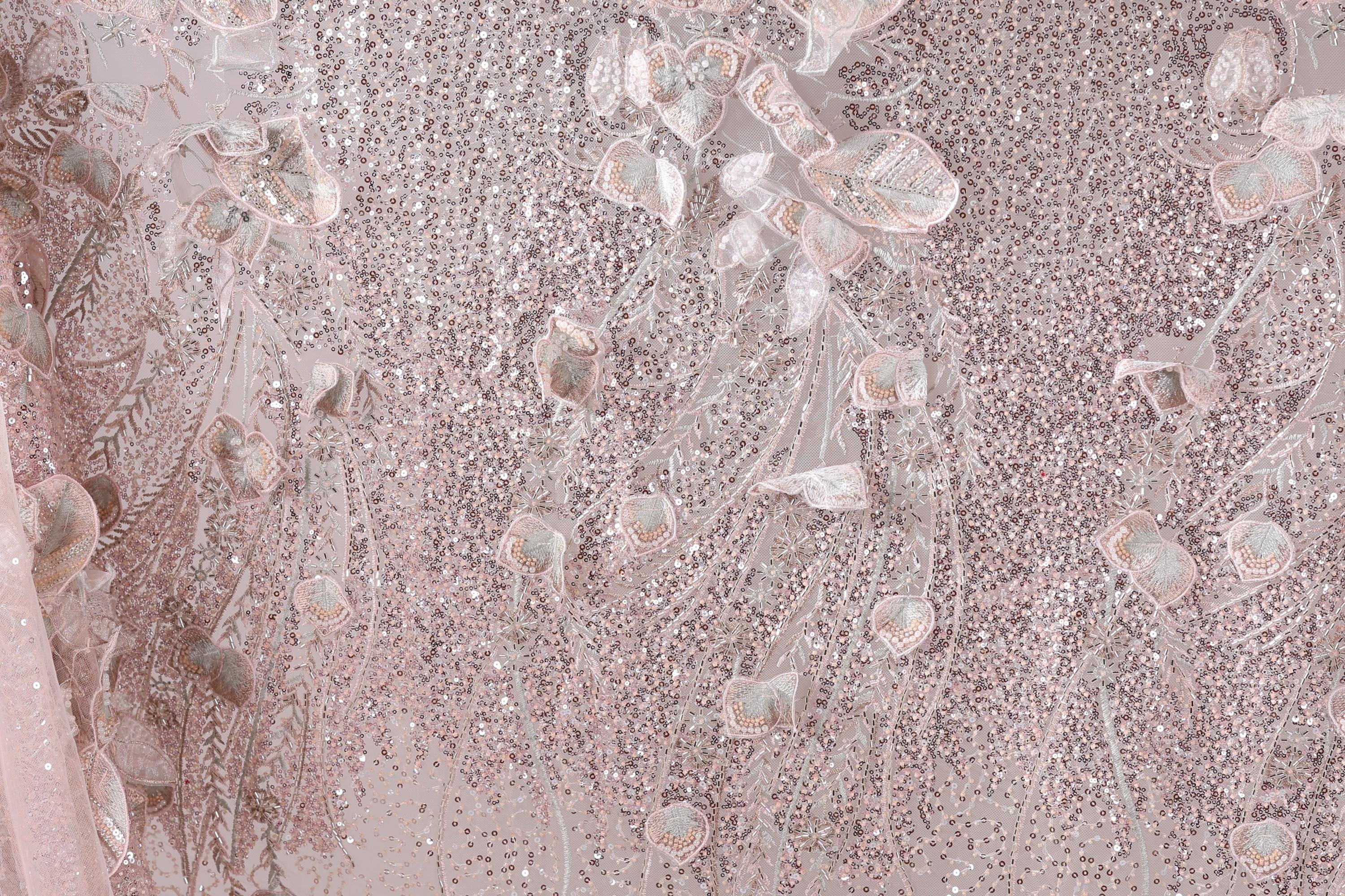 The image is a close-up of a fabric with a pink and white color scheme, featuring a pattern of sequins and beads. The fabric appears to be a sheer or sheer lace material, with a delicate and intricate design.