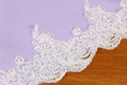 A close-up view of a delicate white lace trim on a purple background.