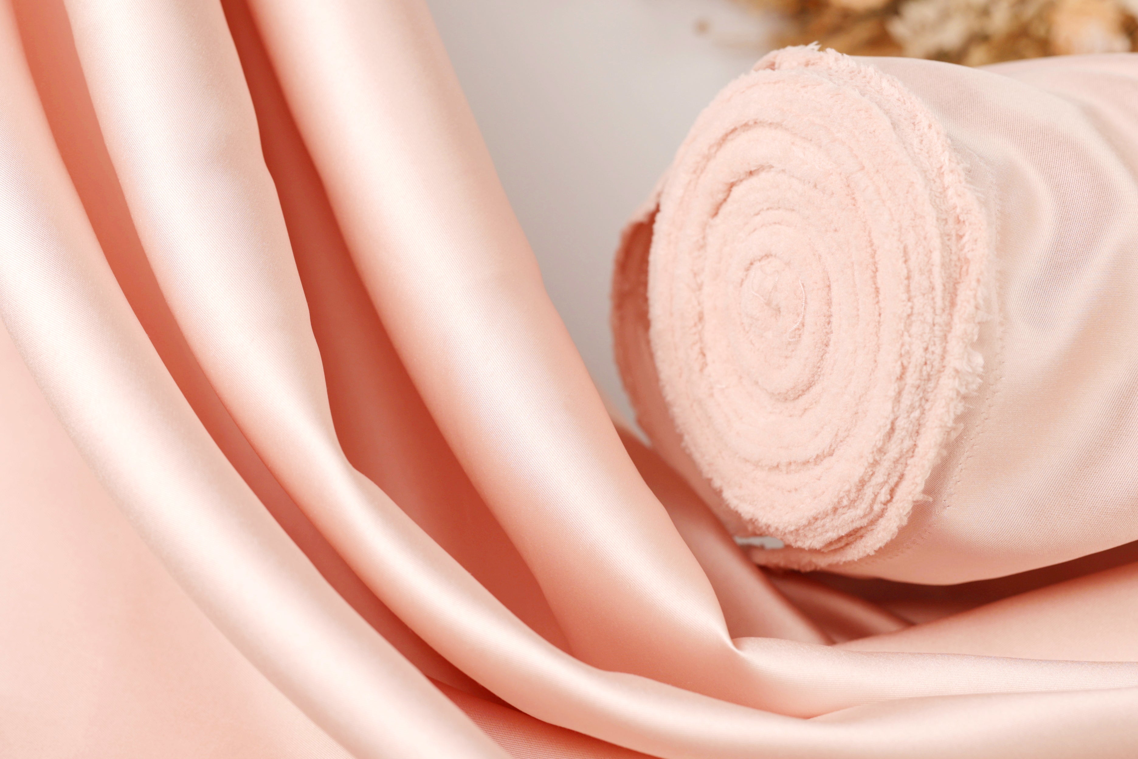 A close-up image of a soft, light pink fabric, possibly silk or satin, with a curled or rolled end visible.