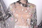 a close-up view of a delicate, sheer fabric with a floral pattern. The fabric appears to be made of sheer material, giving it a transparent and airy appearance. The intricate floral designs on the fabric are visible, adding a touch of elegance and sophistication to the garment.