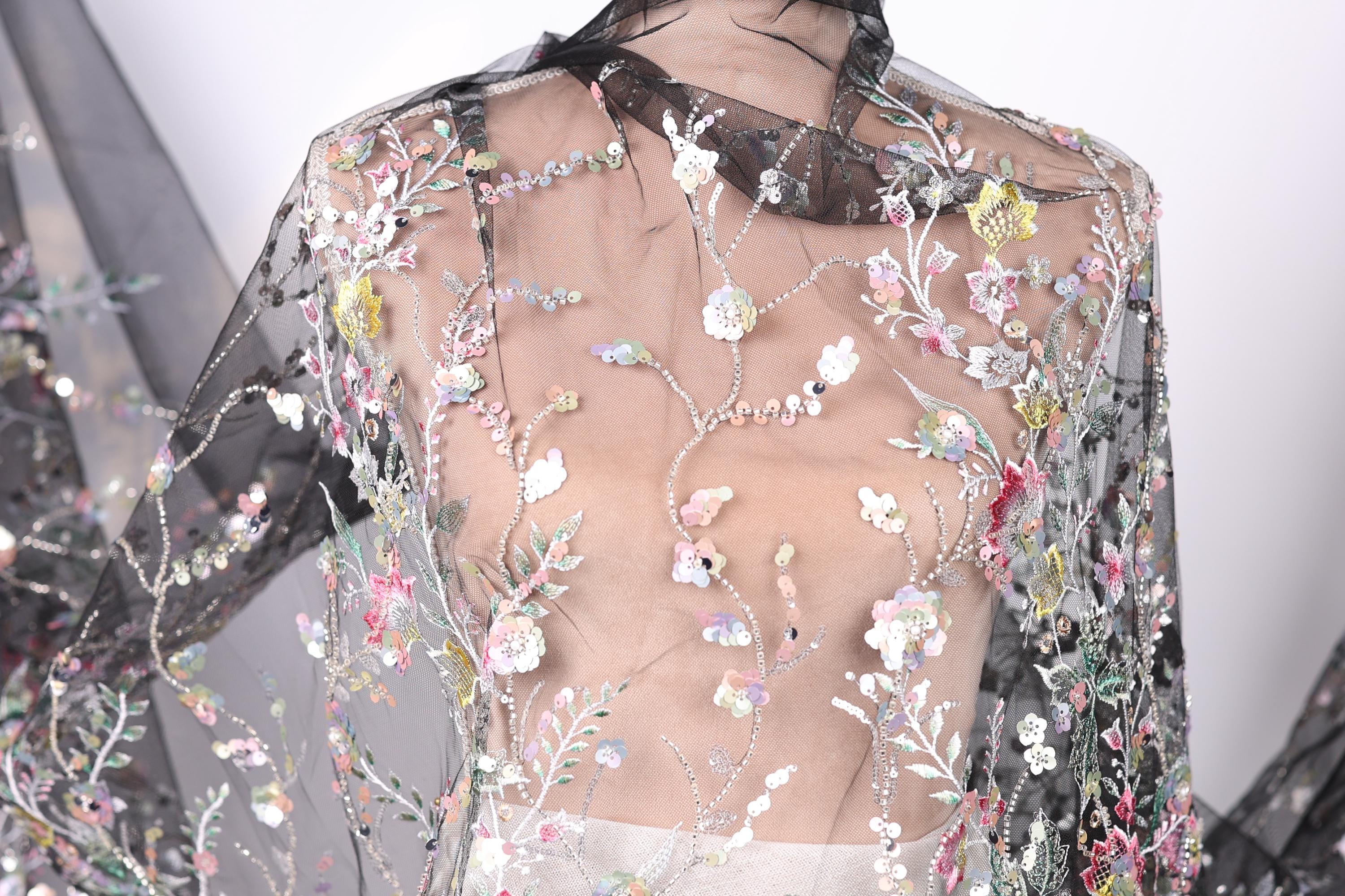 a close-up view of a delicate, sheer fabric with a floral pattern. The fabric appears to be made of sheer material, giving it a transparent and airy appearance. The intricate floral designs on the fabric are visible, adding a touch of elegance and sophistication to the garment.