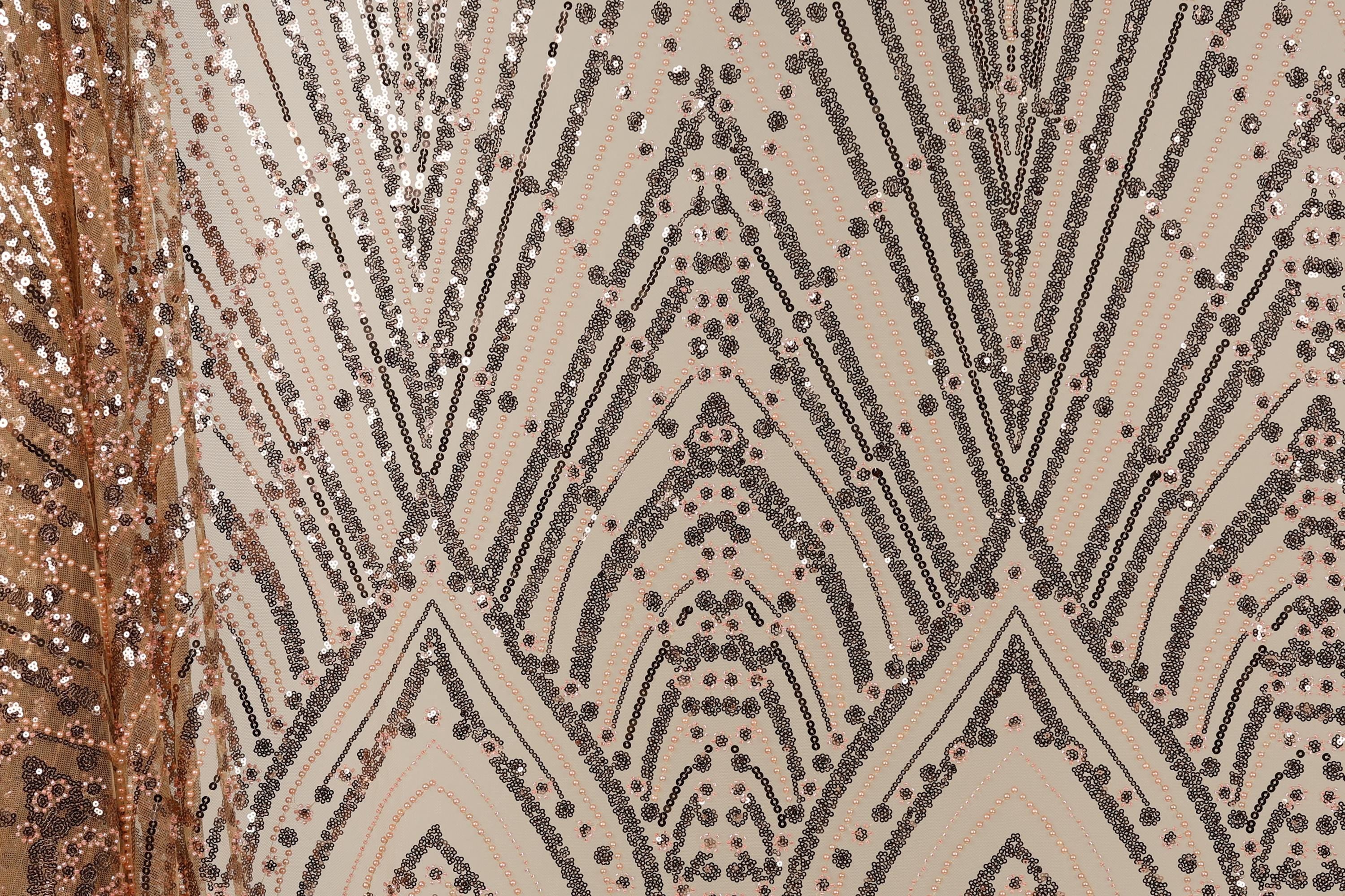 a close-up view of a fabric with a repeating pattern of black and gold sequin designs. The pattern consists of diagonal lines and shapes, creating a visually striking and intricate design. The fabric appears to be a light-colored material, possibly beige or off-white, with the black and gold sequins adding a touch of sparkle and glamour.