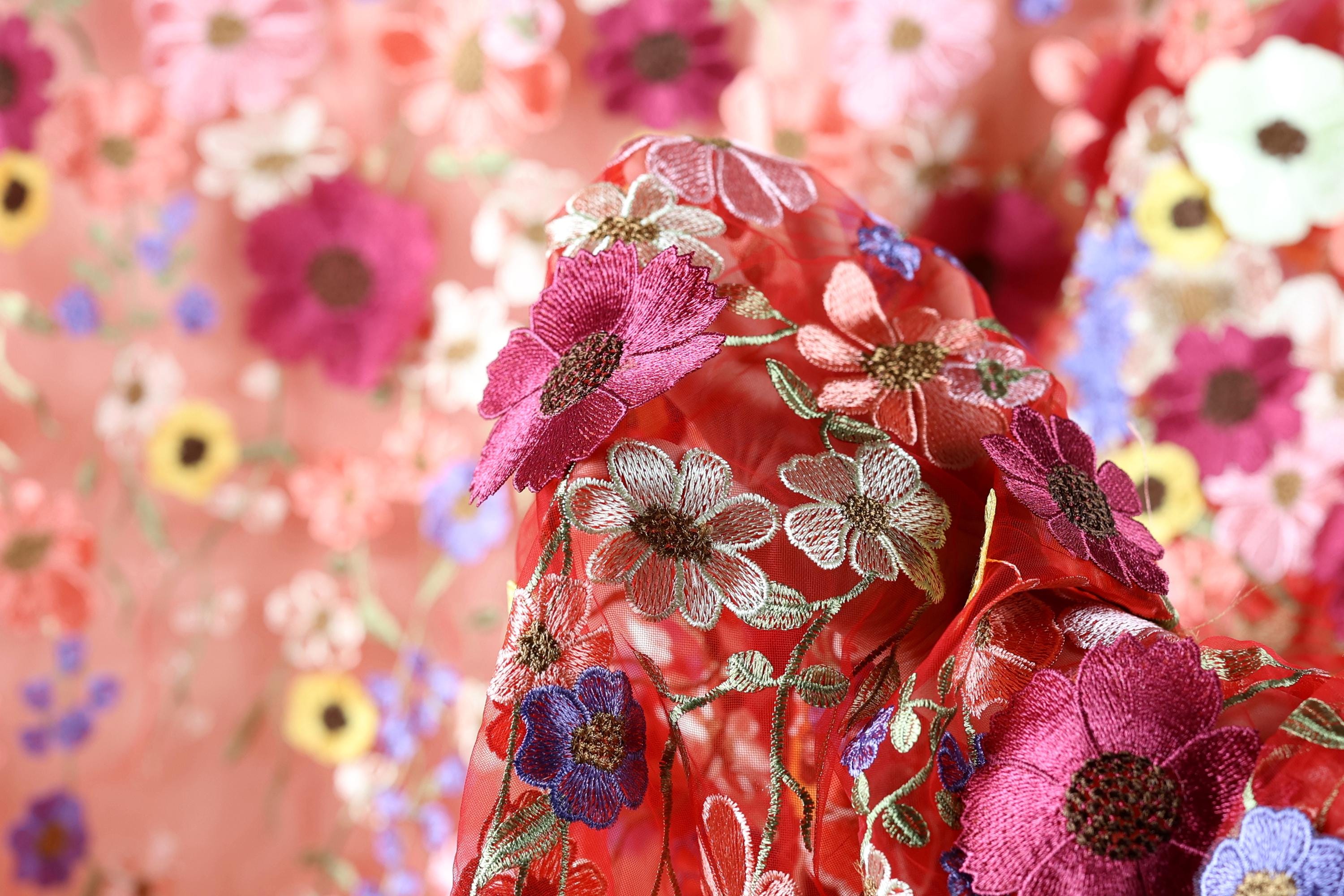 a close-up view of a vibrant red fabric adorned with a variety of colorful flowers, including pink, purple, and yellow flowers, creating a visually striking and intricate design.