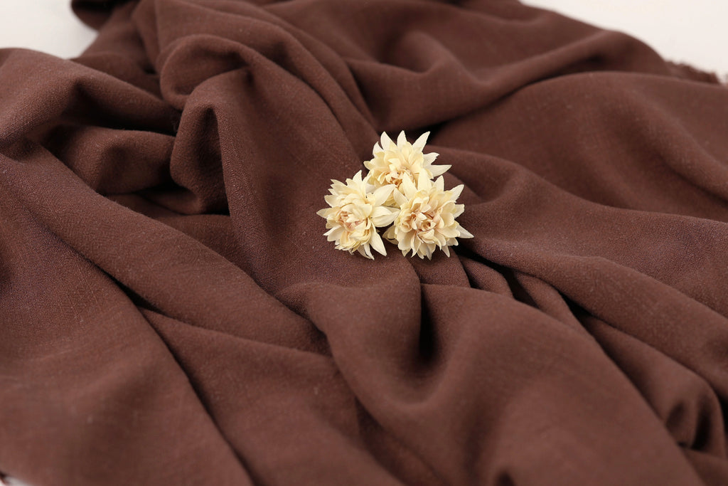 A close-up image of a brown fabric with a small cluster of white flowers resting on it.