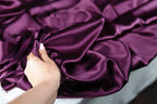 A hand is holding a piece of purple satin fabric, examining it closely.