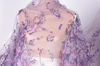 a close-up view of a sheer, purple fabric with a floral pattern. The fabric appears to be made of sheer material, giving it a delicate and airy appearance. The floral pattern is composed of small purple flowers and leaves, creating a visually appealing and intricate design. The fabric is draped over a mannequin, which is positioned in the center of the image. The background of the image is white, which contrasts with the purple fabric and allows it to stand out prominently.