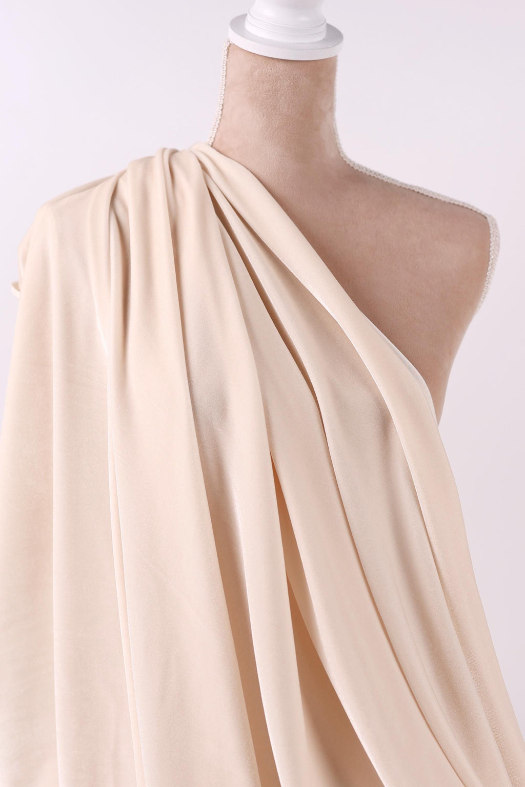 A mannequin wearing a beige, draped fabric draped over its shoulder.