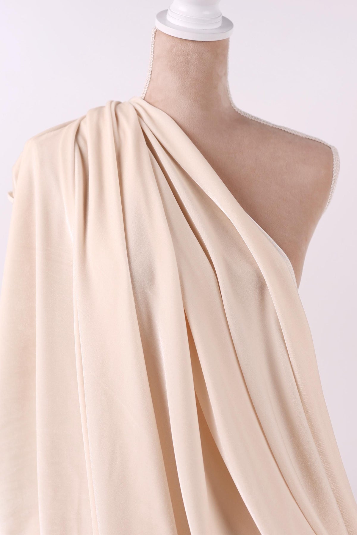 A mannequin wearing a beige, draped fabric draped over its shoulder.