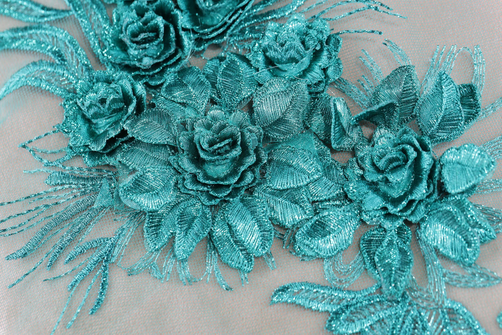 a close-up view of a delicate, intricately designed fabric with a floral pattern. The fabric is adorned with numerous small, shimmering blue flowers and leaves, creating a visually striking and elegant design.